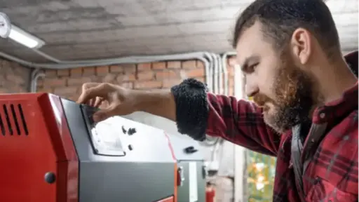 Man adjusting control panel on red industrial machine in brick-walled workshop