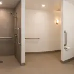 Accessible bathroom with tiled shower, wooden bench, and grab bars under bright lighting