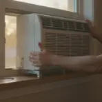 Window air conditioner being installed by person in casual attire with screwdriver nearby