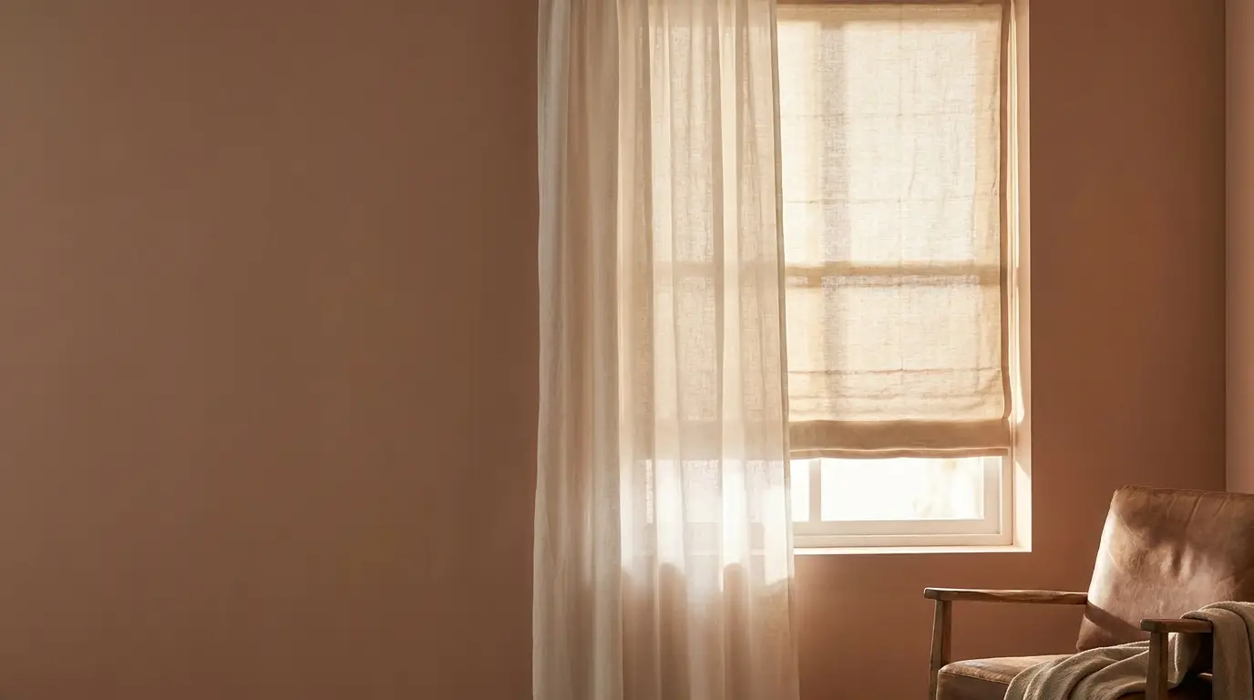 Soft light through sheer curtains over window with beige shade and wooden armchair in cozy room