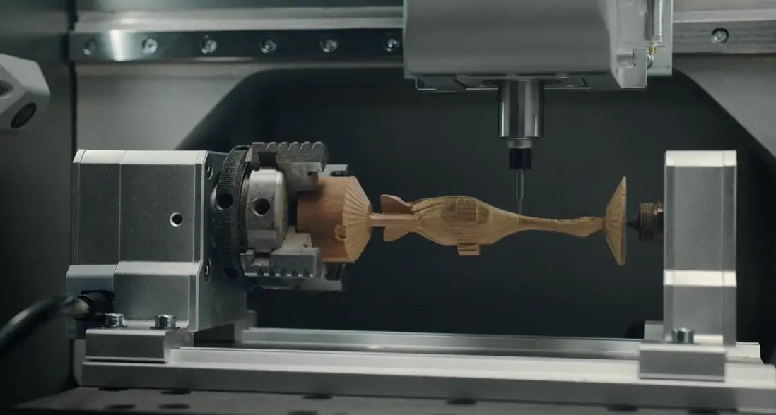 CNC machine carving wooden fish design in industrial setting under cool lighting