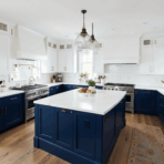 modern white kitchen with navy blue lower cabinets and island white quartz countertops brass hardware hardwood floors and pendant lighting with bright natural light
