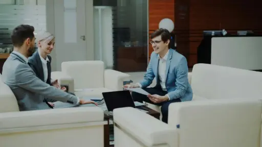 Three people in business attire having a discussion in a modern office lounge