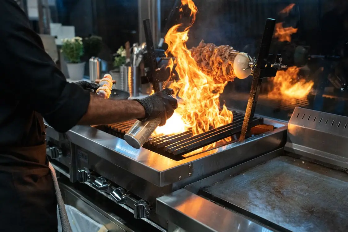 Chef grilling meat over open flame in restaurant kitchen with stainless steel equipment