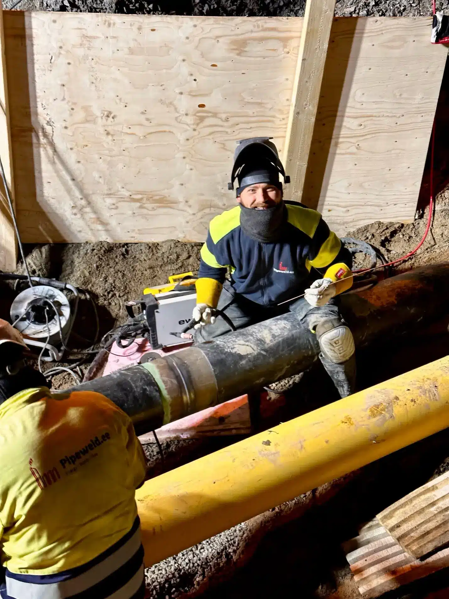 Worker welding large pipe in underground construction site wearing safety gear