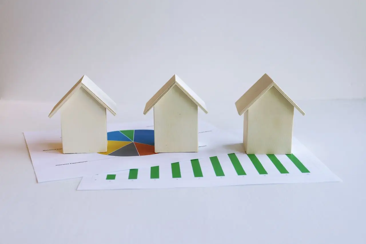 Three miniature wooden houses on financial charts with pie and bar graphs in a bright setting
