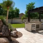 Outdoor kitchen with modern grill and appliances on stone patio under pergola in sunny backyard