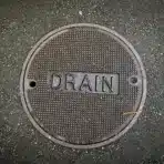 Manhole cover labeled "DRAIN" on textured asphalt pavement