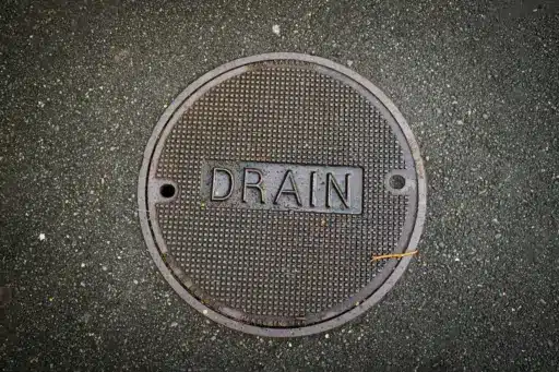 Manhole cover labeled "DRAIN" on textured asphalt pavement