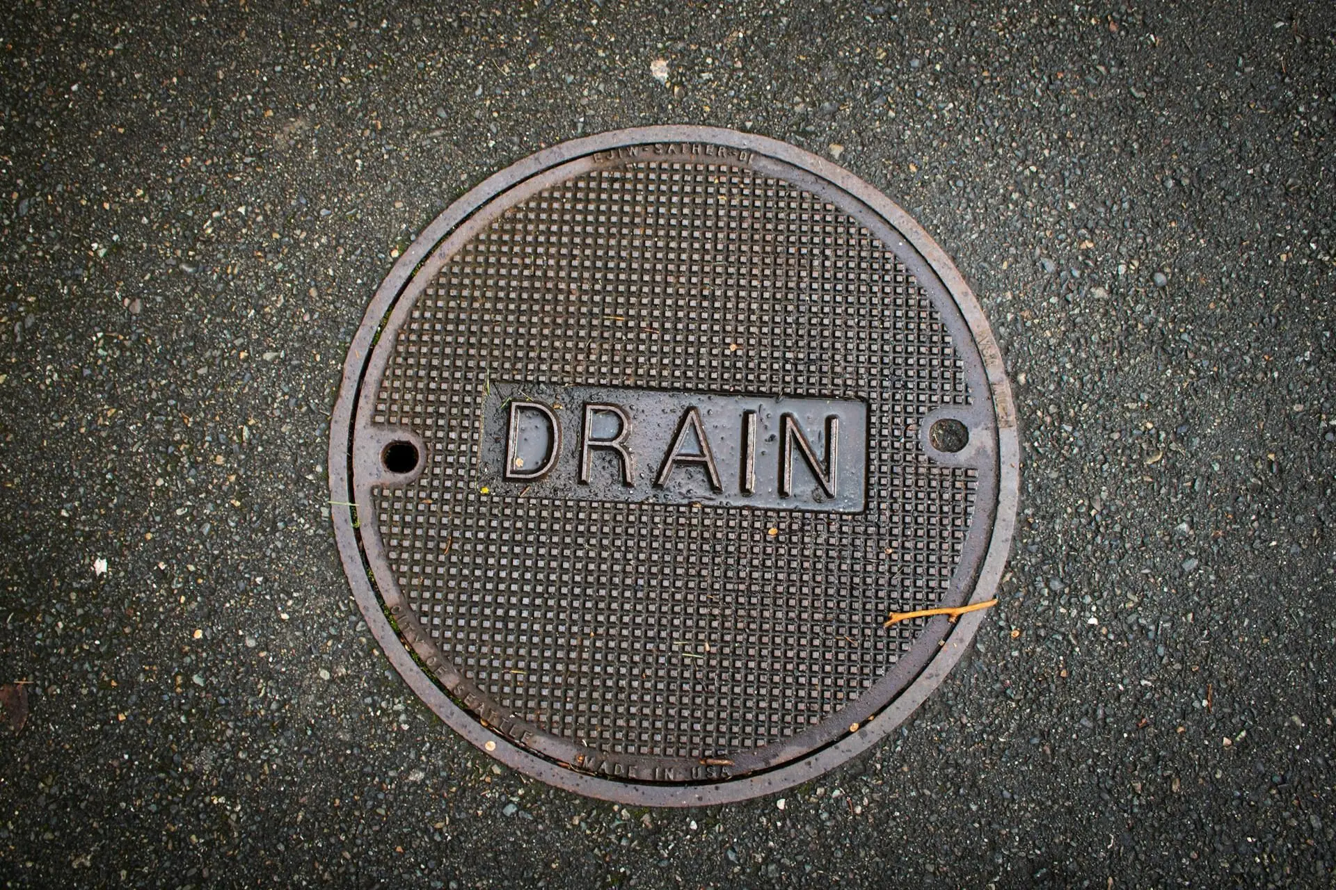 Manhole cover labeled "DRAIN" on textured asphalt pavement