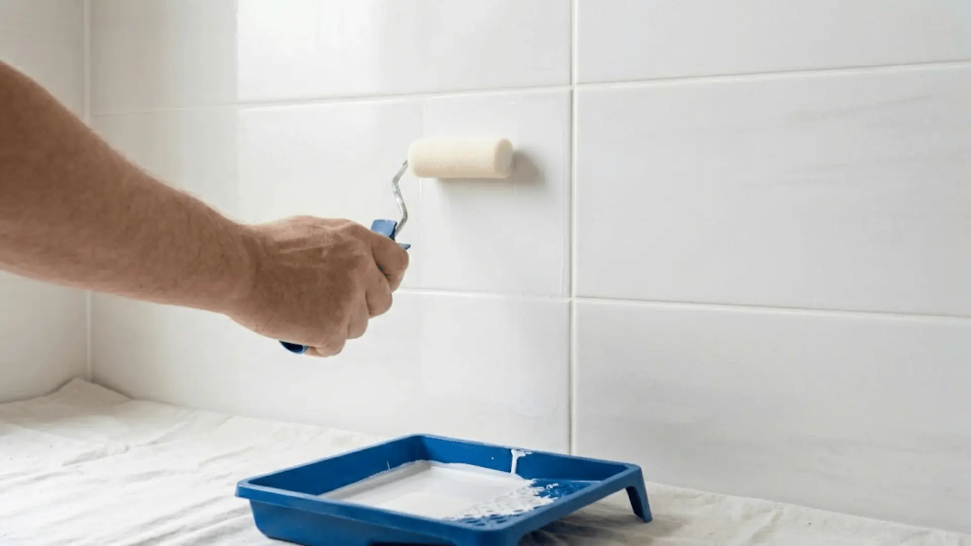 foam roller applying white bonding primer evenly across ceramic bathroom wall tiles