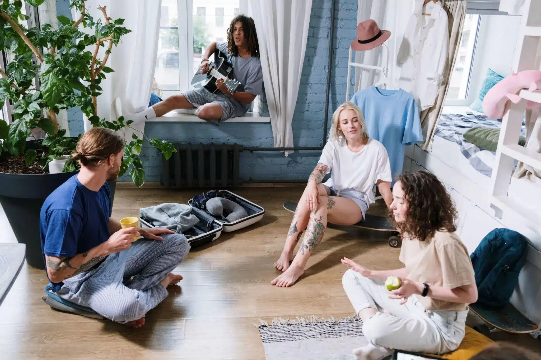 Friends relaxing and playing guitar in cozy bedroom with blue walls and indoor plant