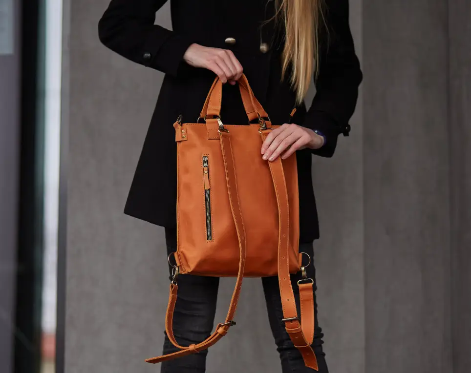 Person holding tan leather backpack against concrete wall background