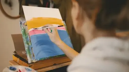 Artist painting colorful abstract scene on canvas in a cozy home studio