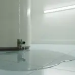 Leaking water heater with water pooling on light blue tiled floor in bright utility room