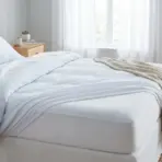 Bed with white sheets and pillows in bright bedroom with wooden furniture and light curtains