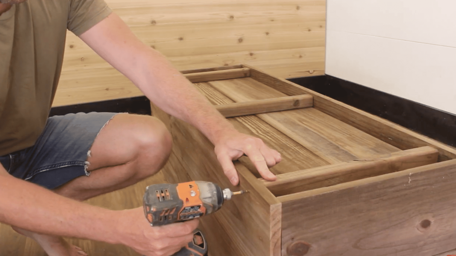 wooden base being affixed to a rectangular frame with drill and screws by a man on wooden furnished floor