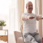 Elderly man doing seated exercises in bright, cozy bedroom with beige curtains