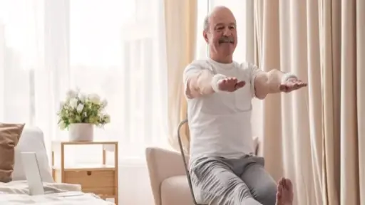 Elderly man doing seated exercises in bright, cozy bedroom with beige curtains