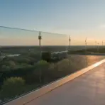 Glass terrace overlooking lush landscape at sunset with clear blue sky and distant horizon