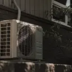 Outdoor air conditioning unit mounted on brick wall with nearby tree shade