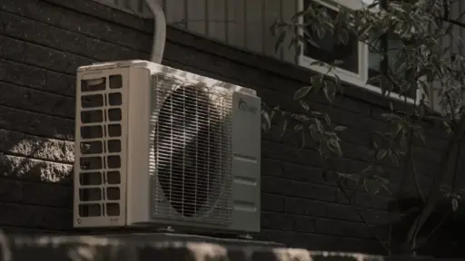 Outdoor air conditioning unit mounted on brick wall with nearby tree shade