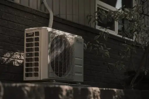 Outdoor air conditioning unit mounted on brick wall with nearby tree shade