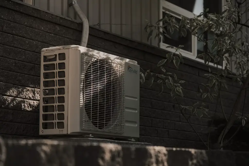 Outdoor air conditioning unit mounted on brick wall with nearby tree shade