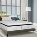 Modern bedroom with plush mattress on grey bedframe, large windows overlooking a tropical beach