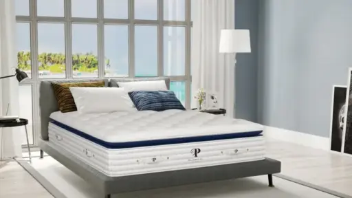 Modern bedroom with plush mattress on grey bedframe, large windows overlooking a tropical beach