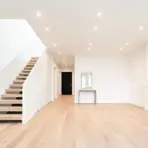 A bright white room featuring a staircase and a cozy fireplace, creating a warm and inviting atmosphere showcasing recessed lighting installation results