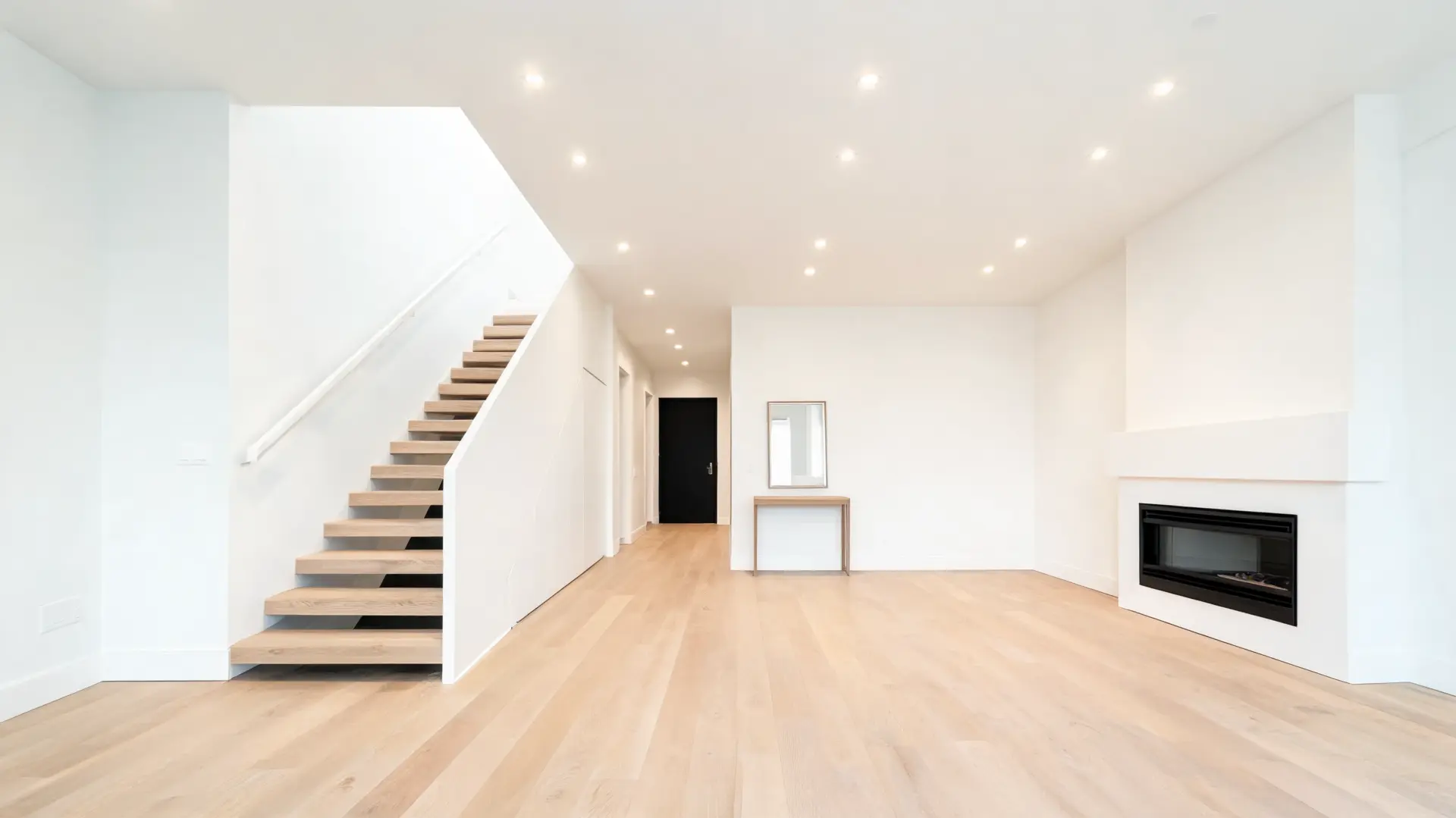 A bright white room featuring a staircase and a cozy fireplace, creating a warm and inviting atmosphere showcasing recessed lighting installation results