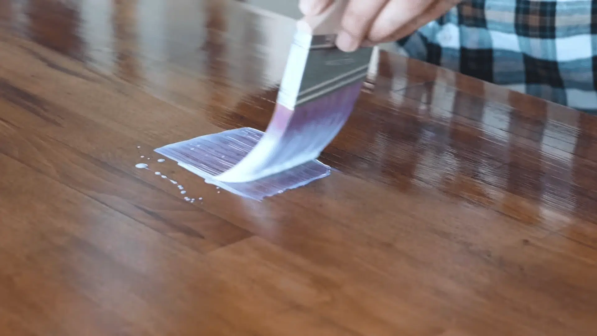 a brush spreads clear finish across a glossy stained wooden tabletop leaving wet strokes on the surface
