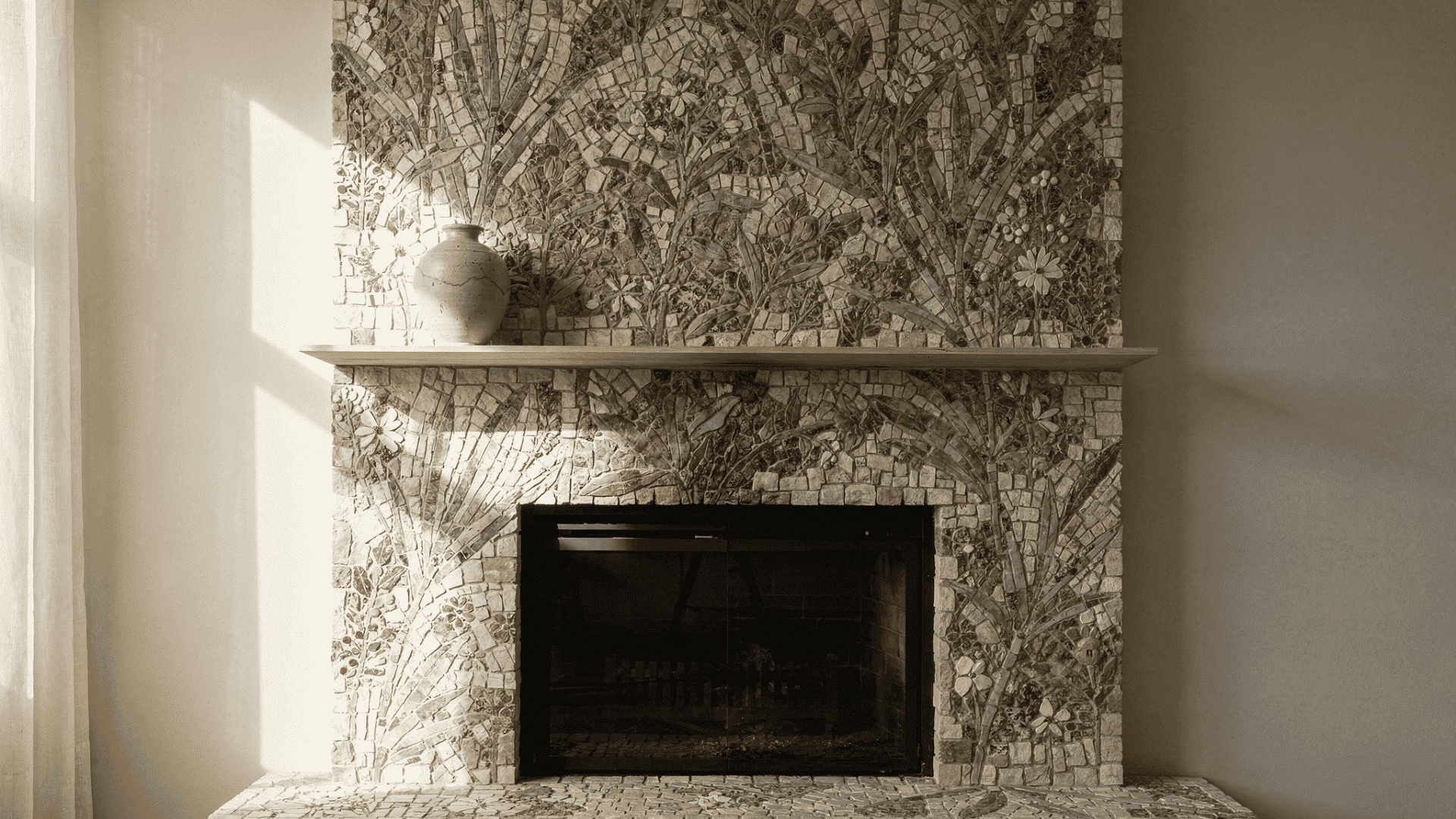 a fireplace with a mosaic tile surround featuring a floral and leaf pattern light colored vase sits on the wooden mantelpiece