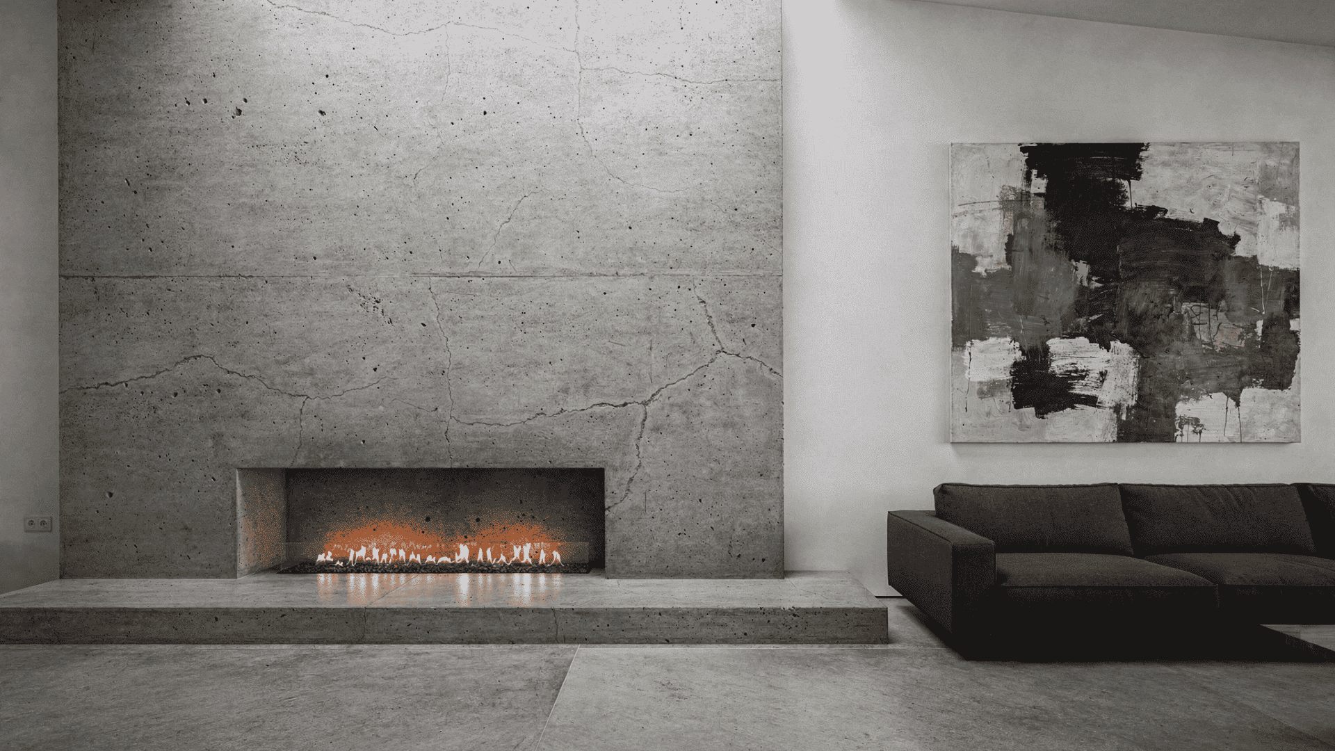 a full width polished concrete fireplace wall with natural cracks and texture housing a wide linear gas burner with a raised concrete hearth platform in a minimal room with a dark sectional sofa a