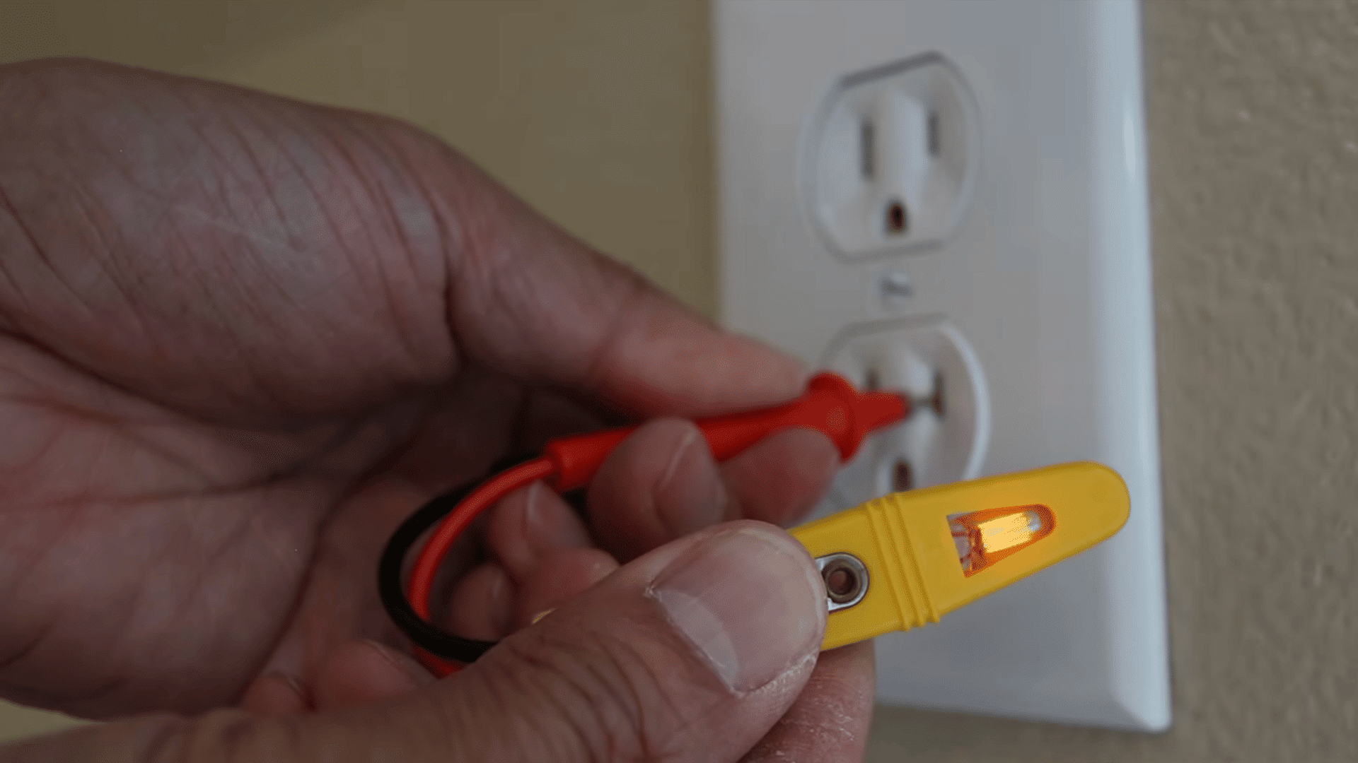 a hand using an active yellow voltage tester on a new power outlet hanging onto a beige wall