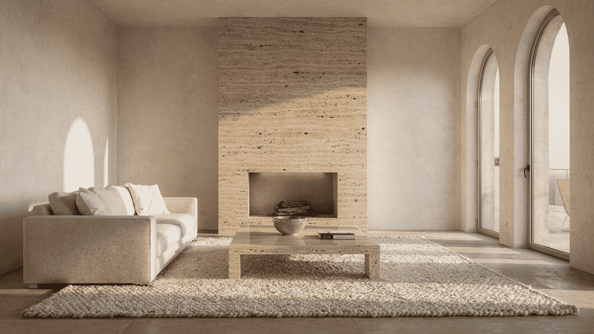 a minimal mediterranean style living room with a floor to ceiling travertine clad fireplace chimney breast in warm cream with natural pitting and a simple open firebox beside tall arched windows
