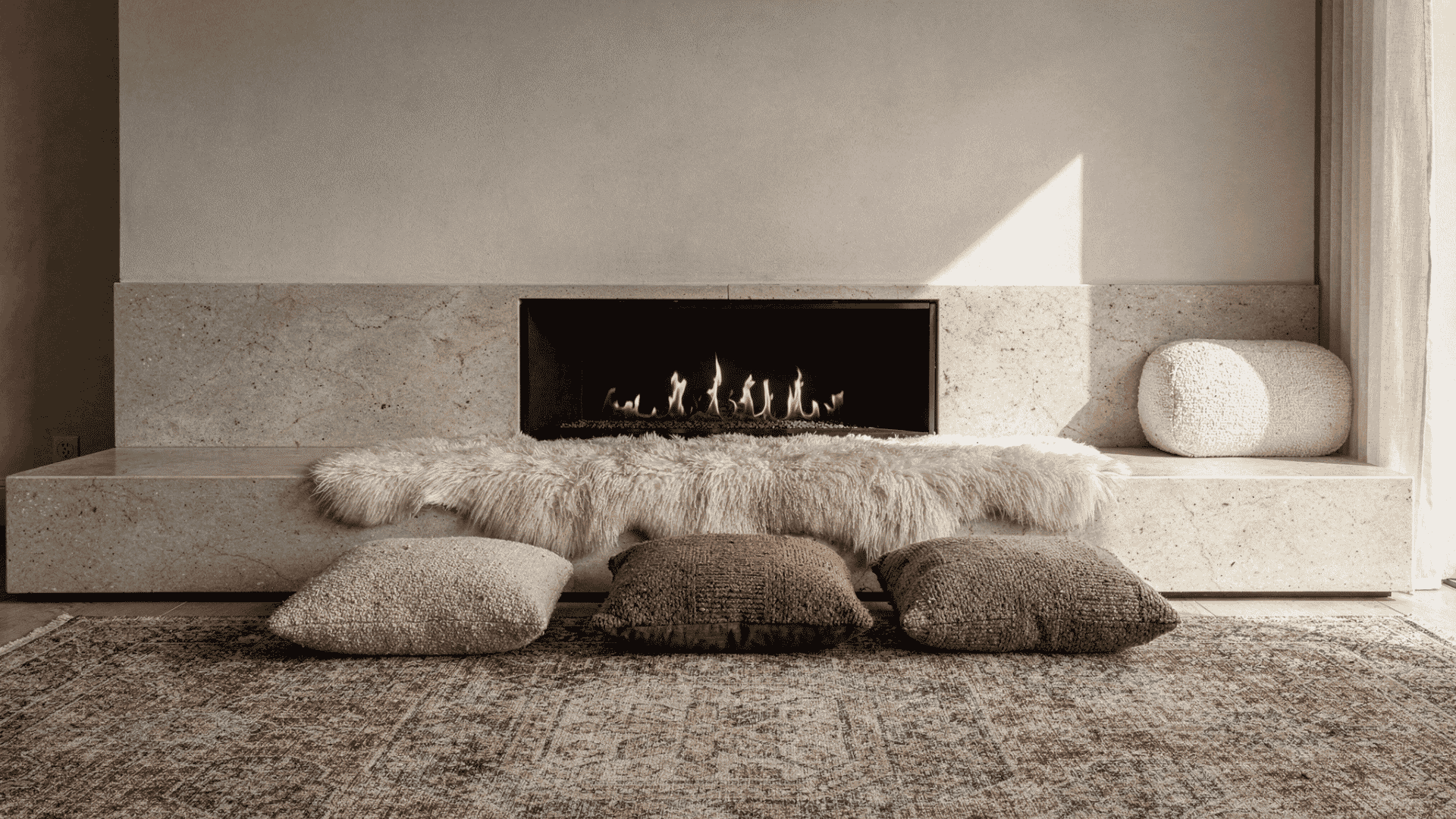 a modern fireplace with a minimalist design featuring a sleek black firebox a stone hearth and a fluffy white sheepskin rug three textured floor cushions are arranged in front of the hearth on a p