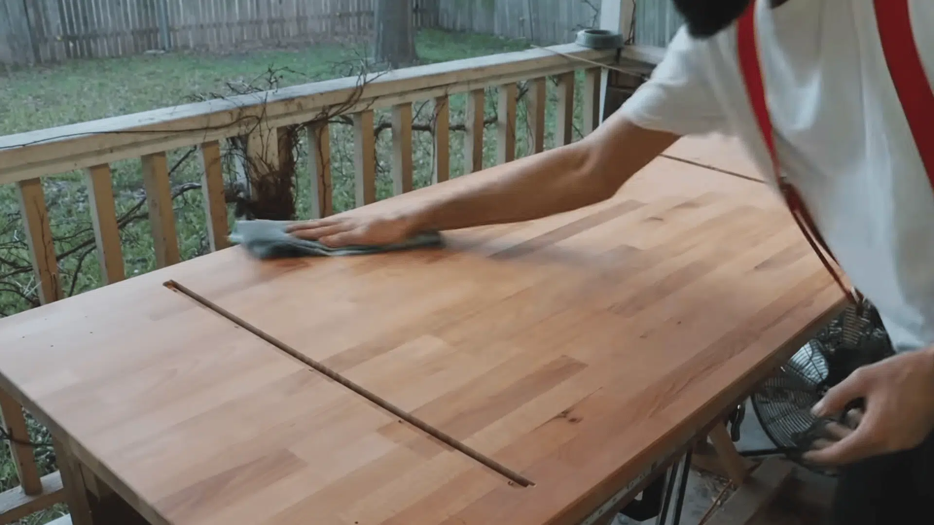 a person wipes dust from a wooden tabletop with a cloth after sanding it on a porch workbench