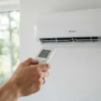 hand holding remote control to adjust wall-mounted air conditioner set to 21 degrees
