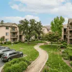 apartment courtyard with balconies parked cars green lawn curved walkway mature trees shrubs and garden beds