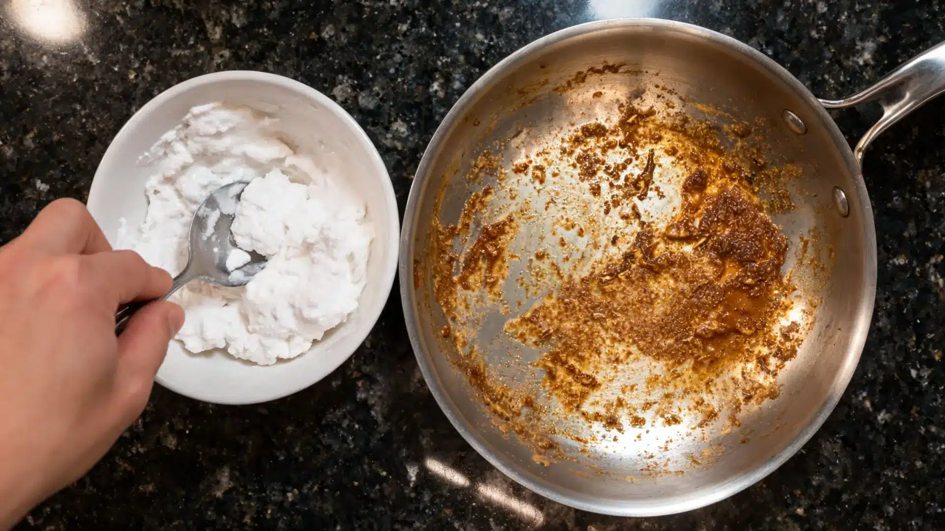 hand mixing wet baking soda paste in white bowl with spoon beside a greasy stainless steel frying pan on dark counter