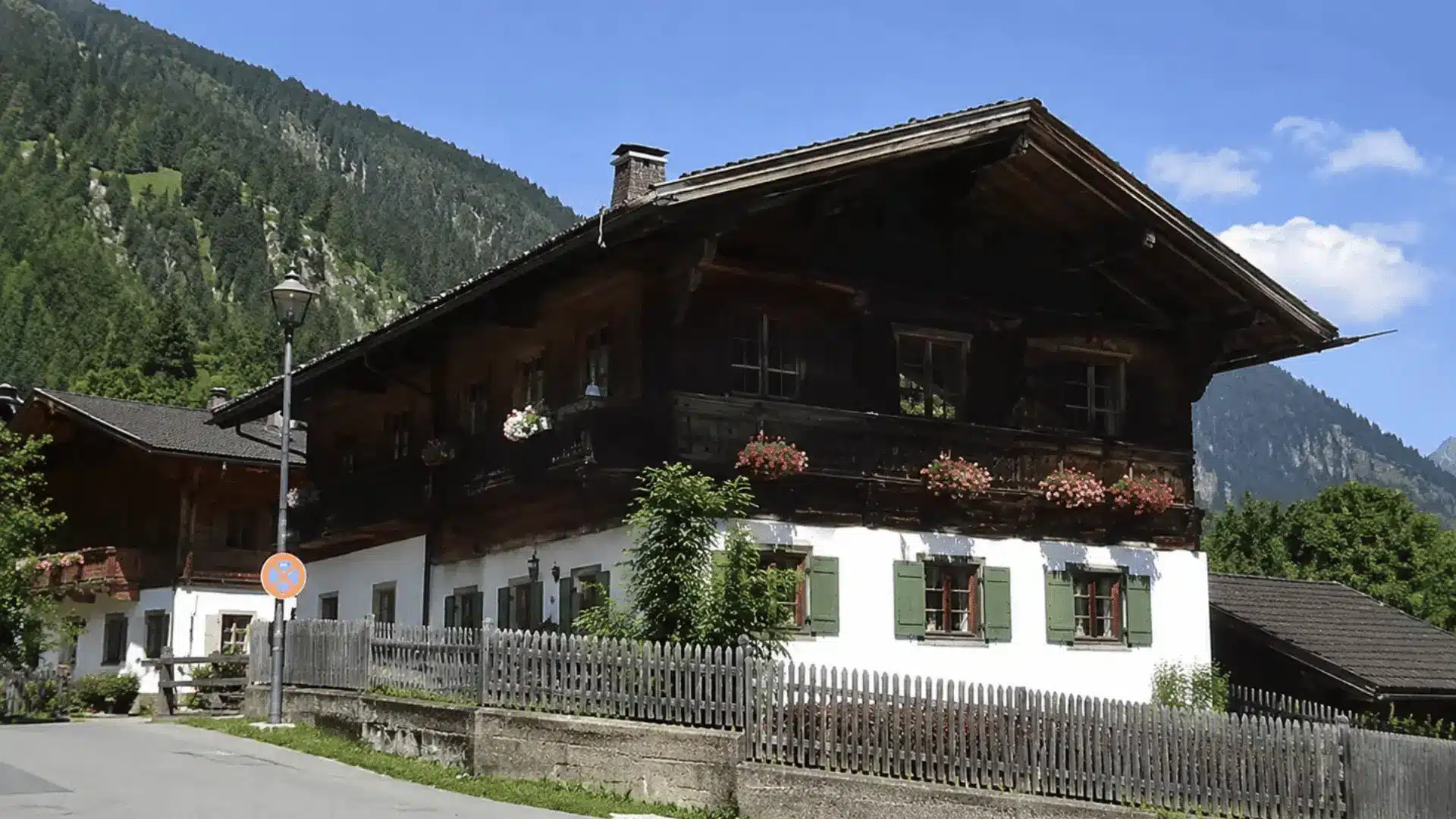 alpine farmhouse with dark wood balcony flower boxes green shutters and mountains behind