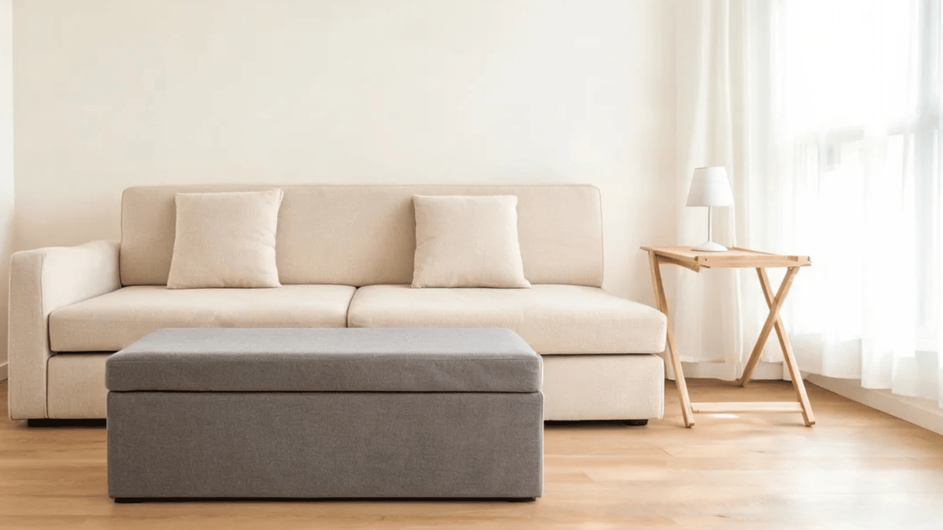 beige sofa with gray ottoman wooden side table and lamp in bright minimalist room