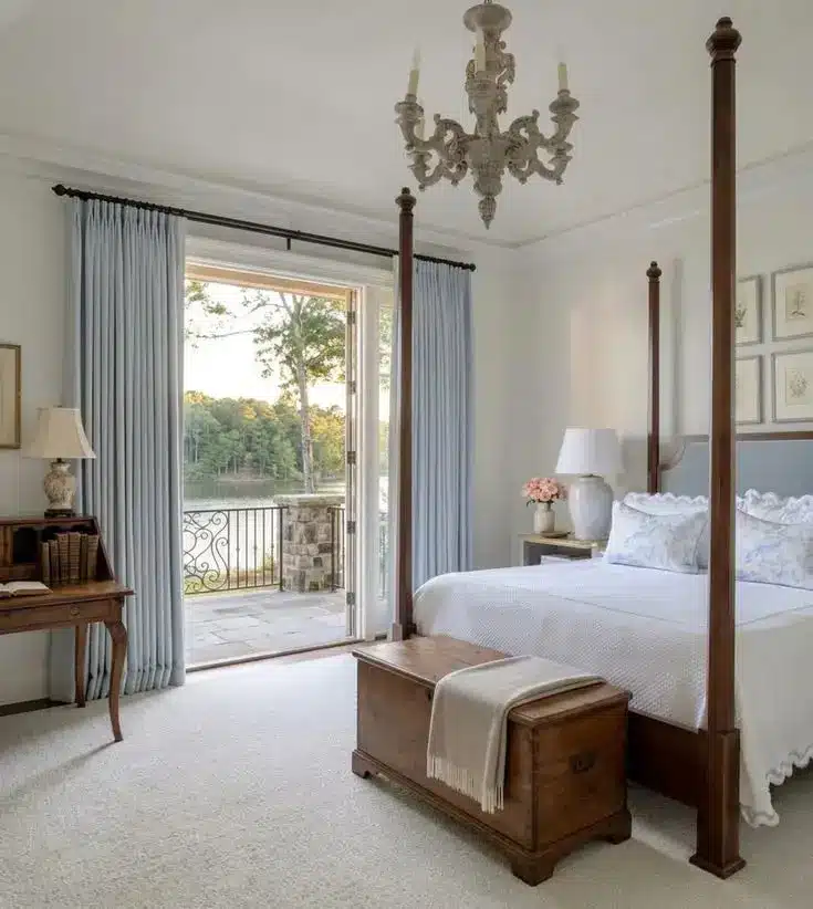 Elegant bedroom with four-poster bed and chandelier overlooking outdoor patio with scenic view