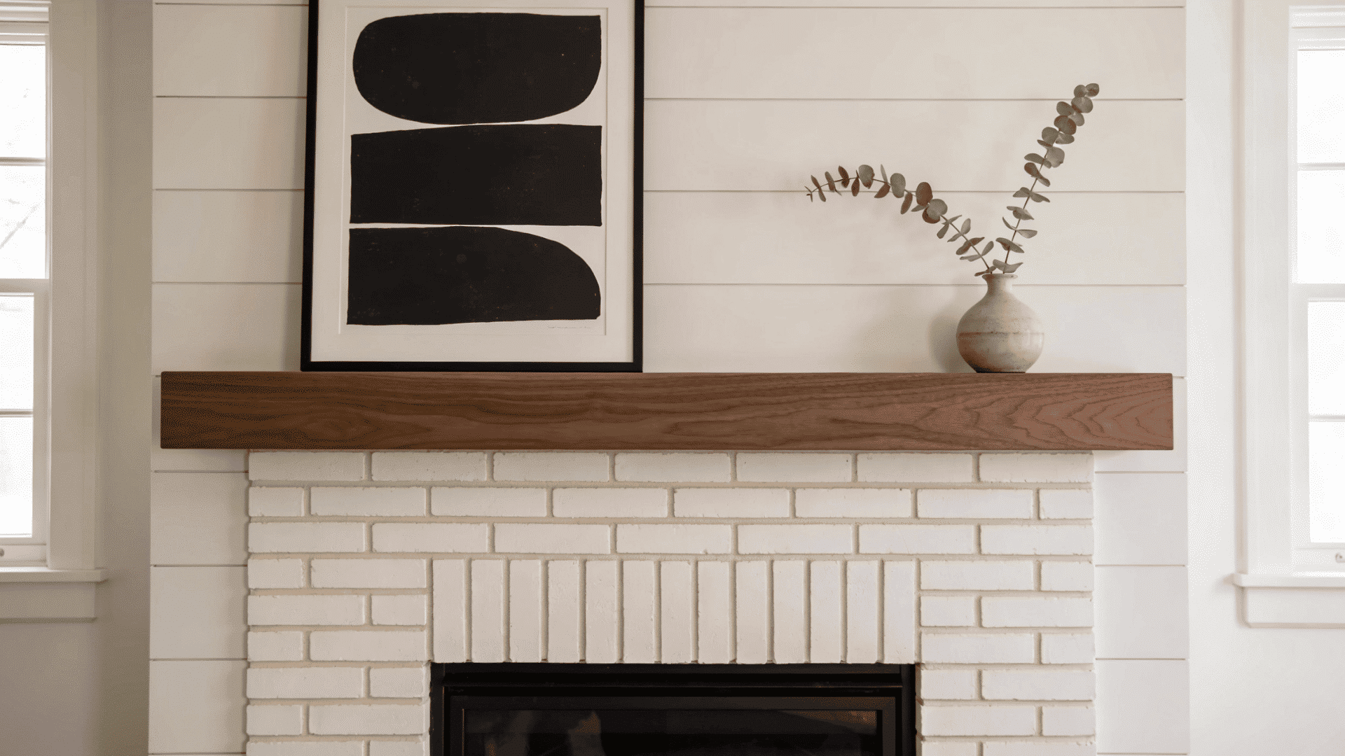 _brick styled fireplace showing the fireplace painted white with a clean wood mantel and abstract art