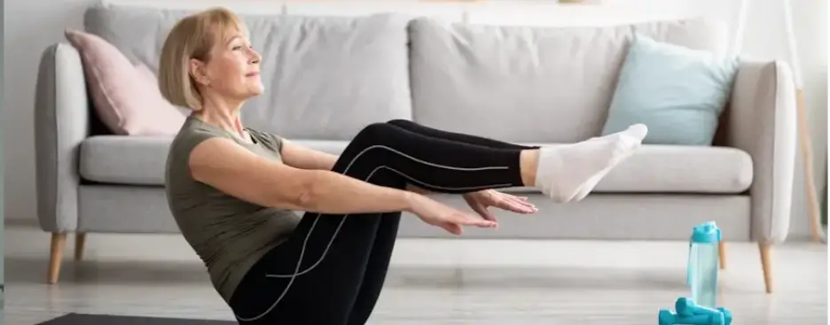 Woman practicing yoga pose on mat in living room with gray sofa and cushion in background