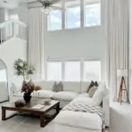 Spacious living room with white sectional sofa, wooden coffee table, and large windows with sheer curtains