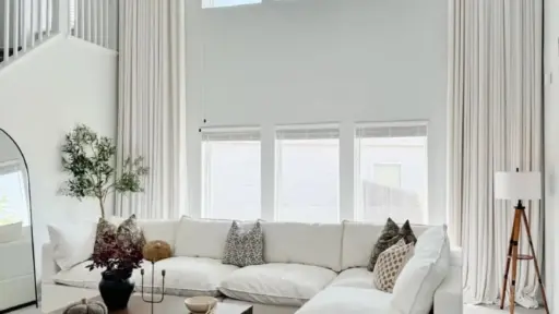 Spacious living room with white sectional sofa, wooden coffee table, and large windows with sheer curtains