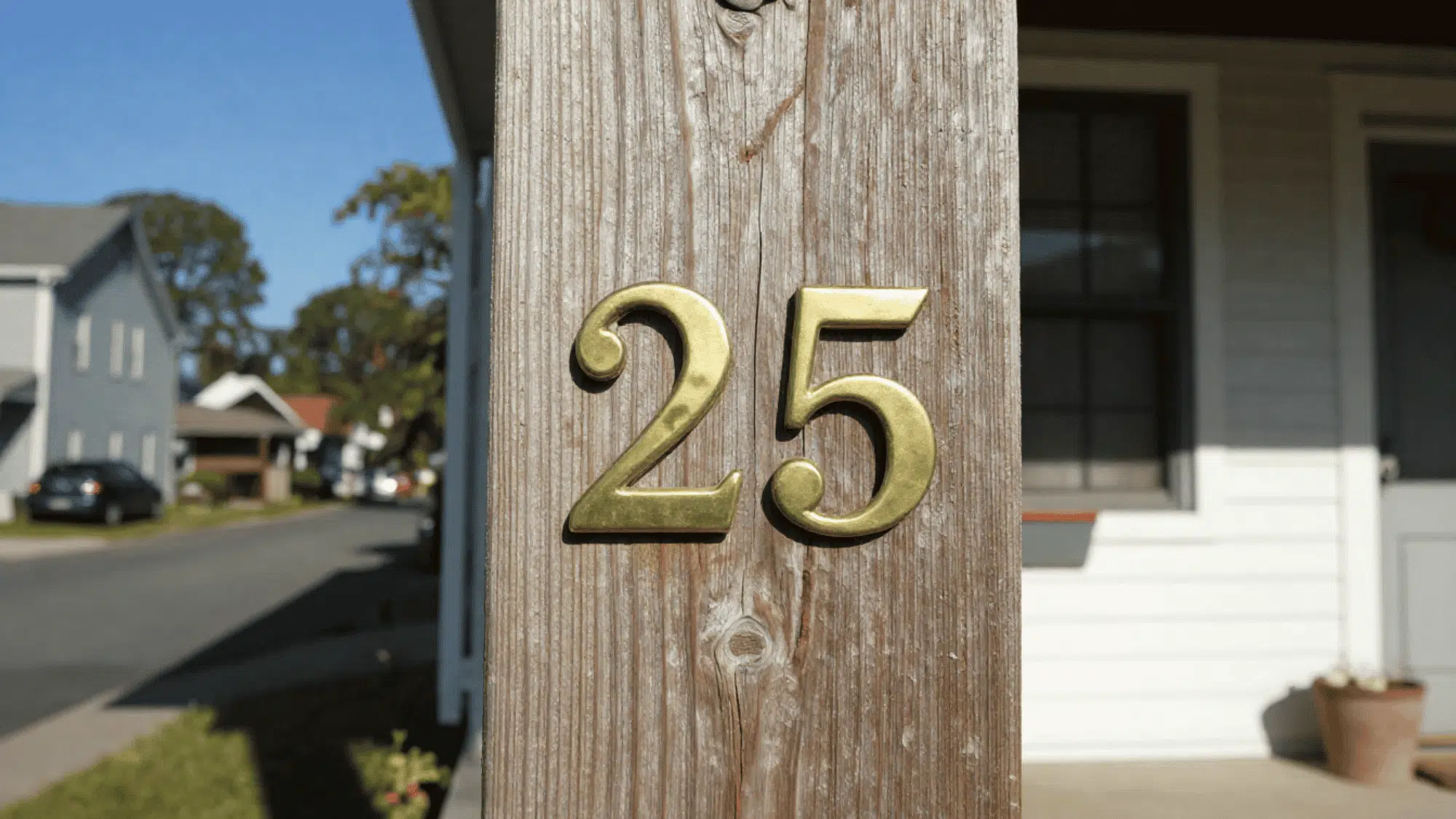 close up of new matte brass house numbers on a rustic wooden porch pillar with natural wear in uneven afternoon sunlight